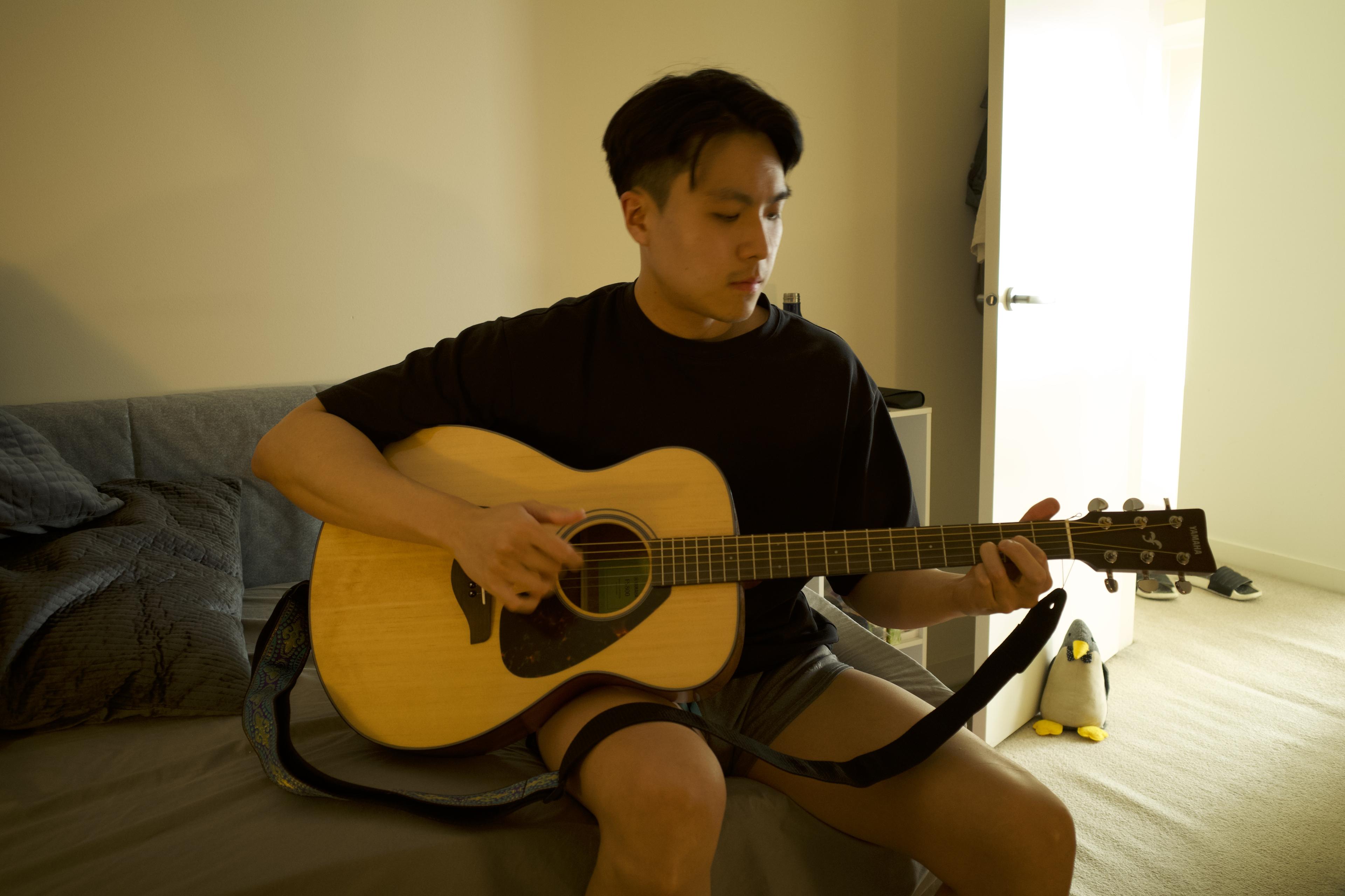 Sean sitting on a couch, looking down while playing an acoustic guitar